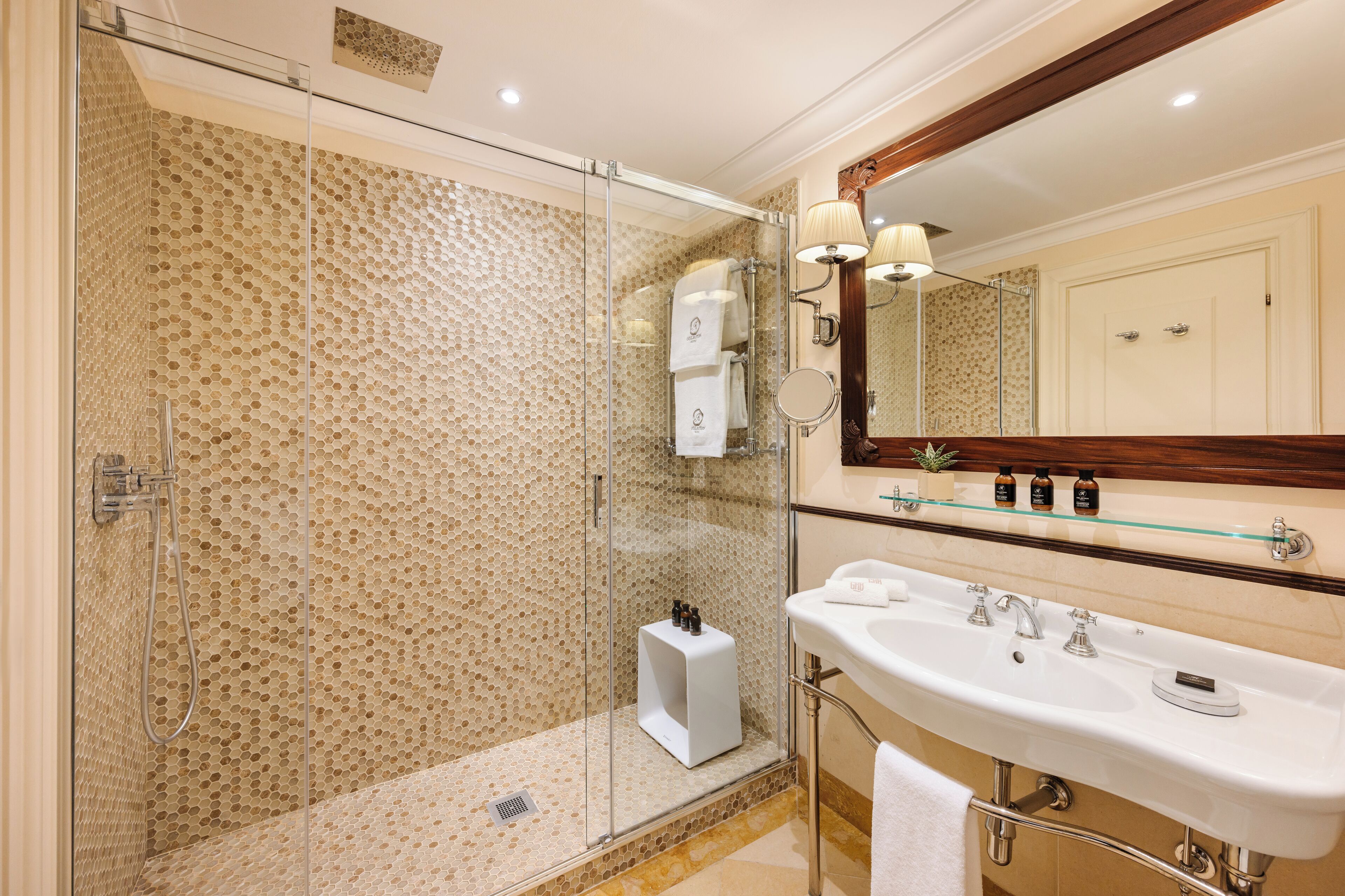 A modern bathroom with a glass-enclosed shower, a large sink, and a mirror with a wooden frame.