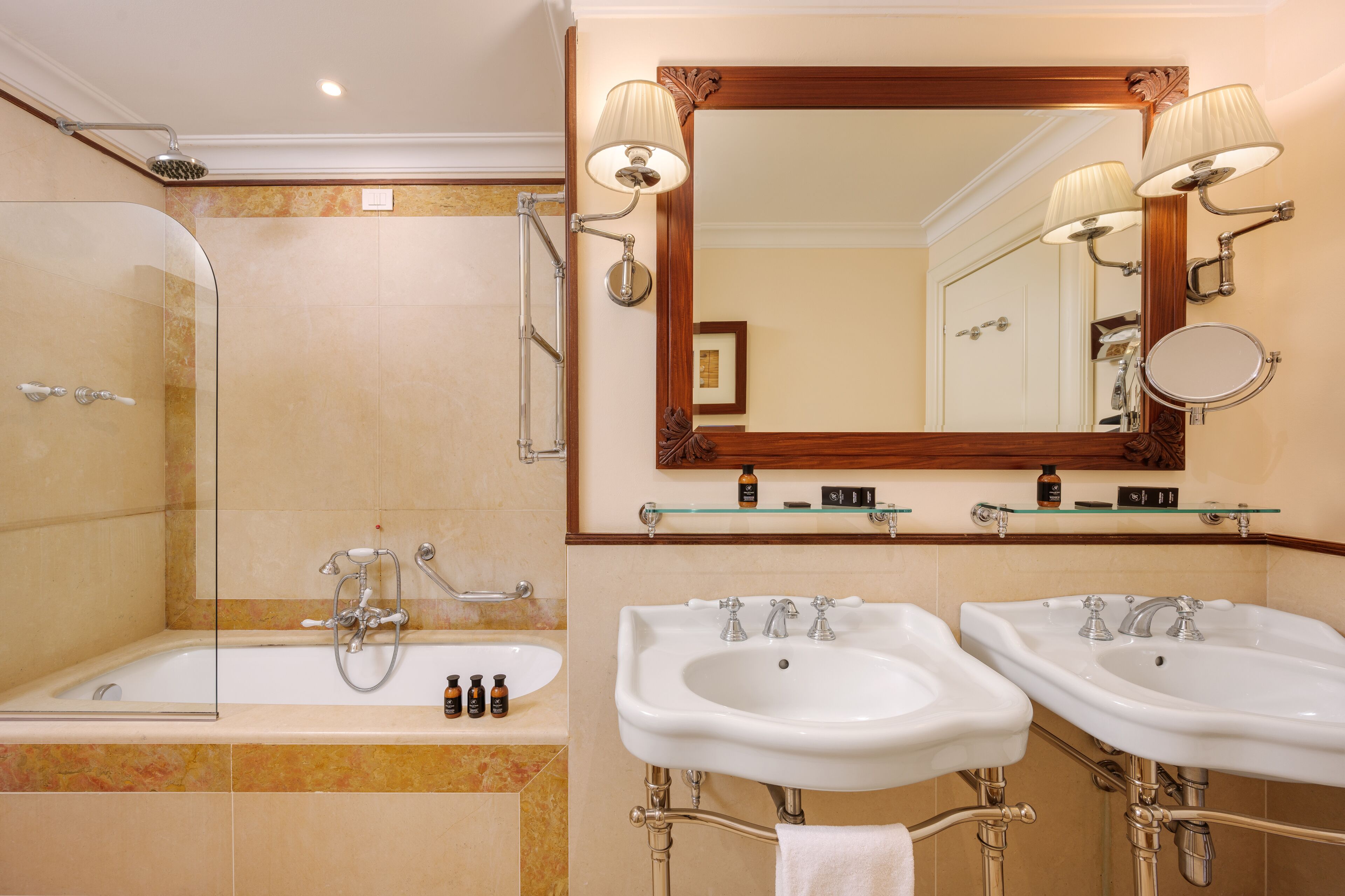 Un baño con ducha acristalada, dos lavamanos y un espejo grande con apliques de pared.