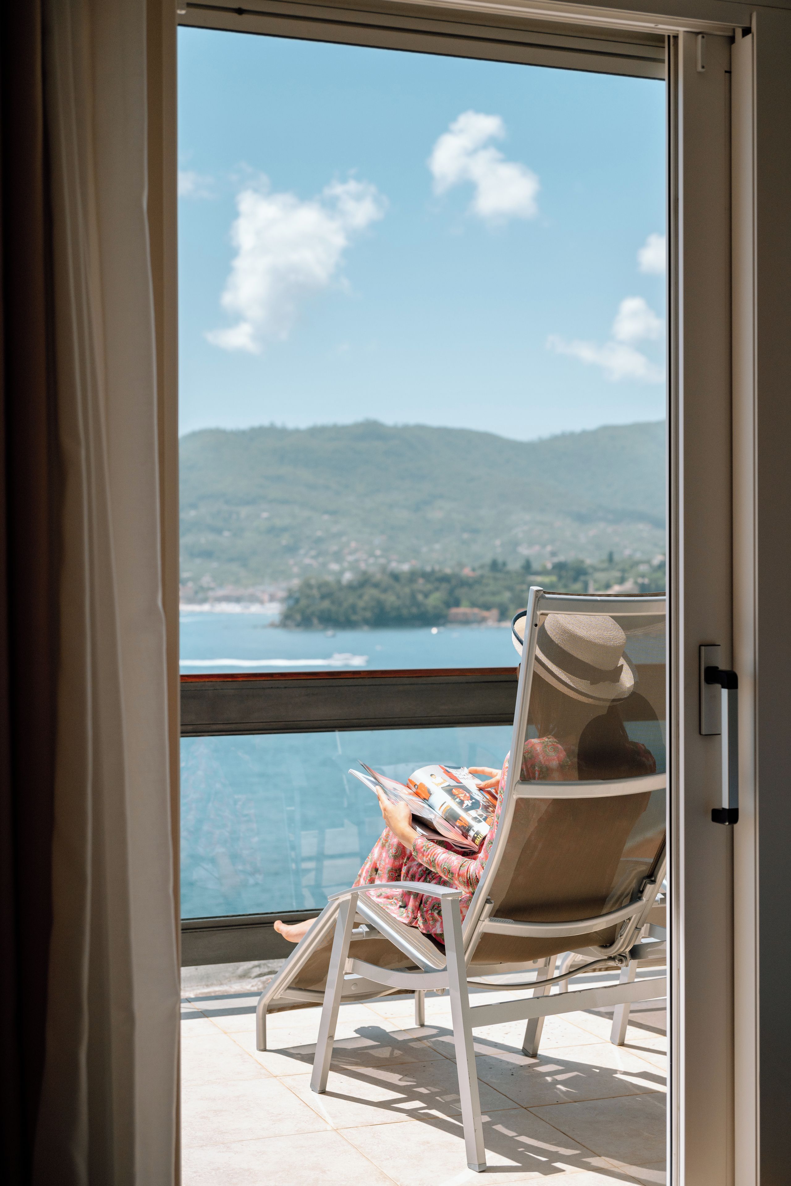 A balcony with a chair and a table, overlooking a body of water and hills.