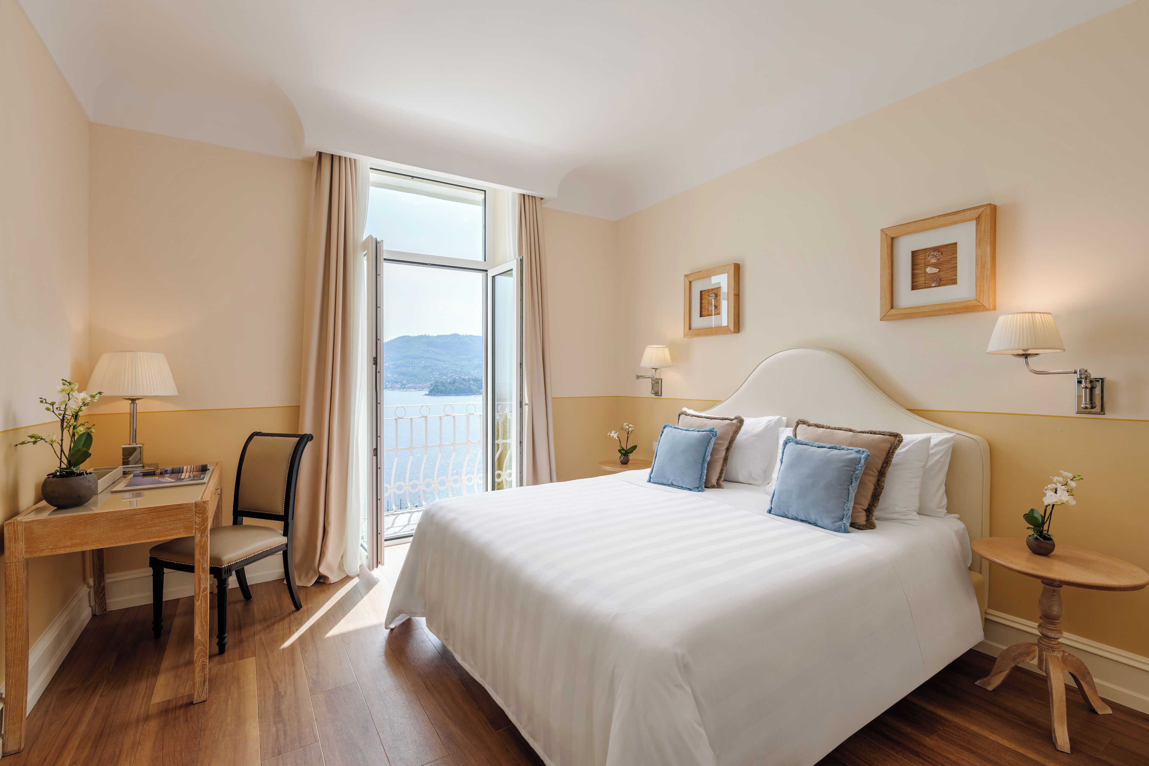 A hotel room with a large bed, a desk with a chair, a small table with a lamp, and a view of the outdoors.