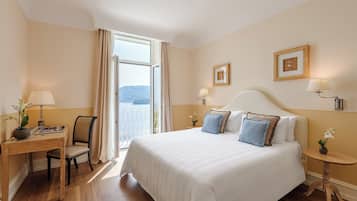 A hotel room with a large bed, a desk with a chair, a small table with a lamp, and a view of the outdoors.