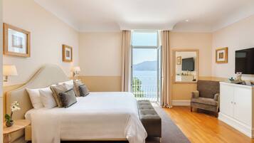 Una habitación de hotel con una cama grande, un sillón pequeño, un televisor y un balcón con vista al mar.