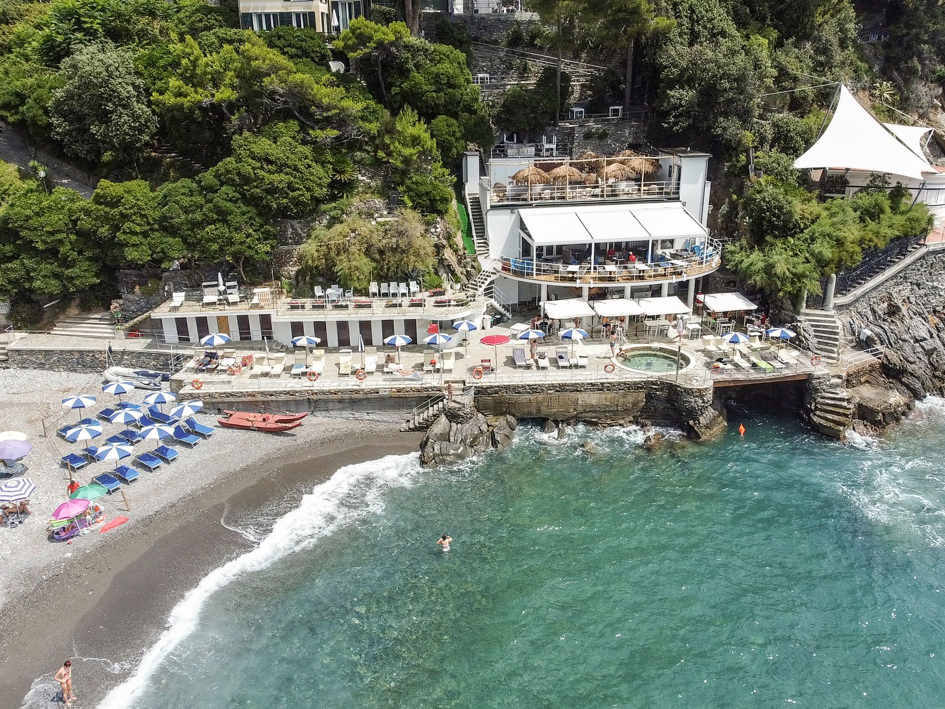A coastal hotel with a pool, beach umbrellas, and a rocky shoreline.