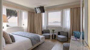Une chambre d’hôtel avec un lit, deux fauteuils, une petite table avec un vase et une grande fenêtre avec des rideaux.