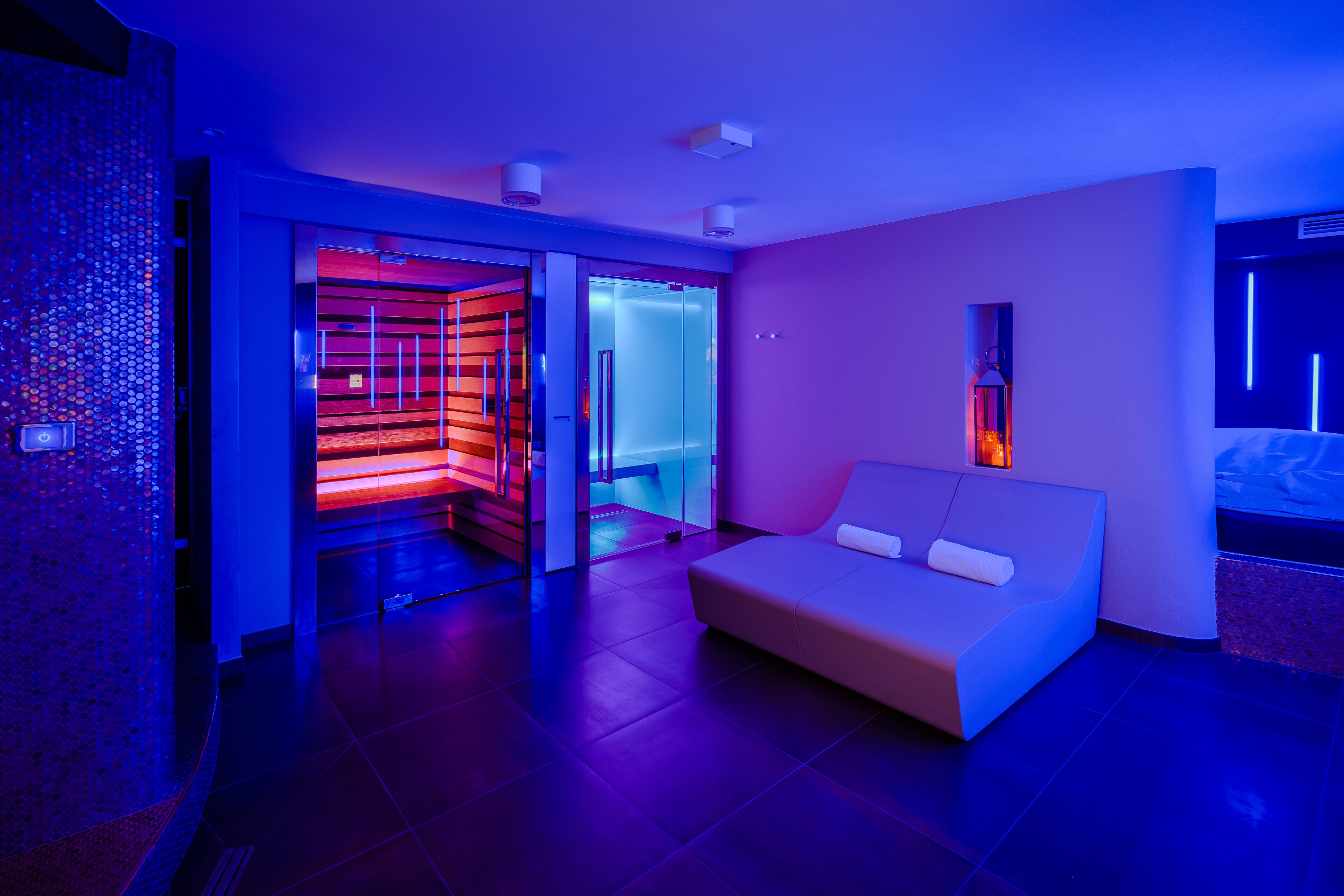 Ein modernes Hotelzimmer mit einer Couch, einer Glastür zu einem Badezimmer und einer Wand mit einem geometrischen Muster.