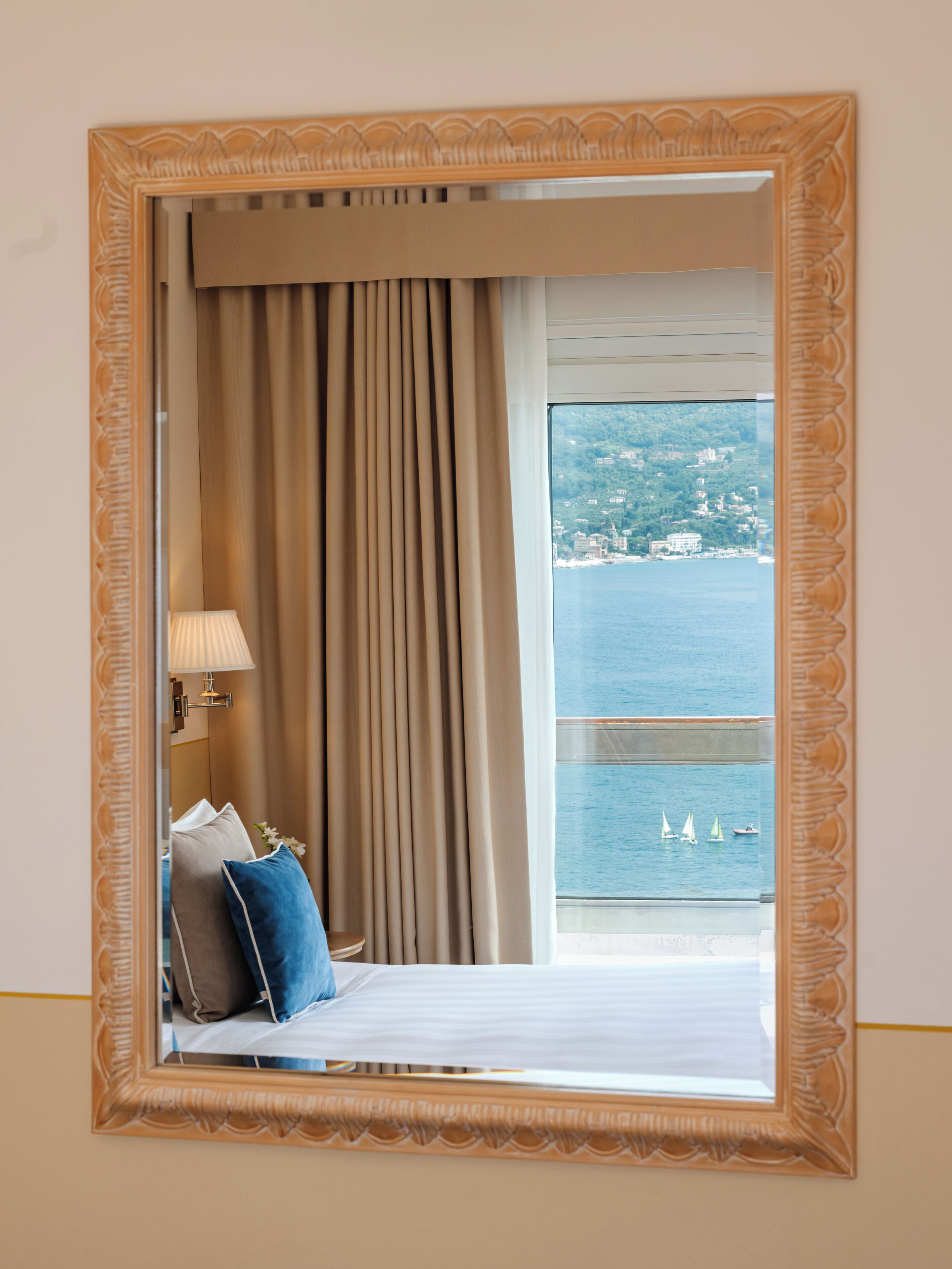 A hotel room with a bed, a nightstand, a lamp, and a view of the sea through a window with curtains.