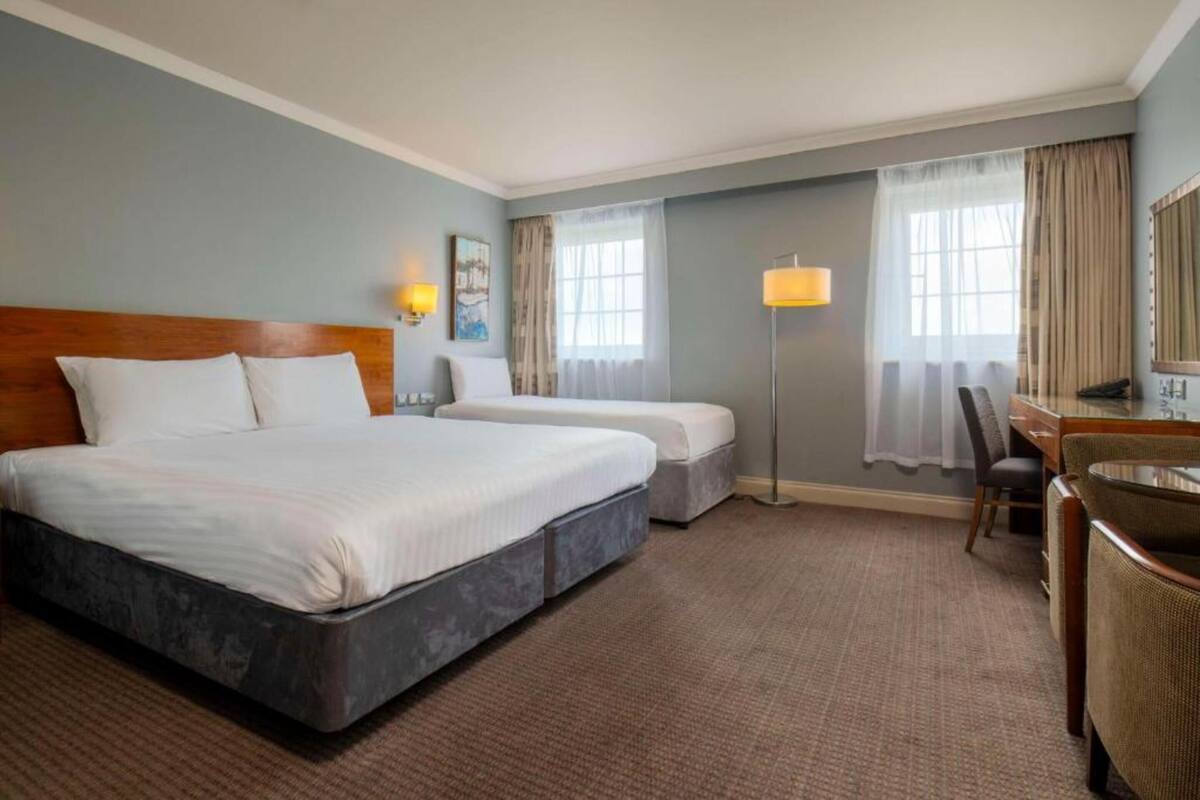 Una camera d'albergo con un letto grande, una scrivania, due sedie, una lampada e una finestra con tende.