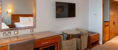 Une chambre d’hôtel comprenant un lit, un bureau avec un miroir, une télévision, une petite table ronde avec des chaises et une armoire.