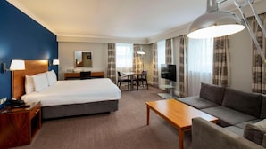 Ett hotellrum med en säng, en soffa, ett skrivbord, en stol, en tv och en lampa.