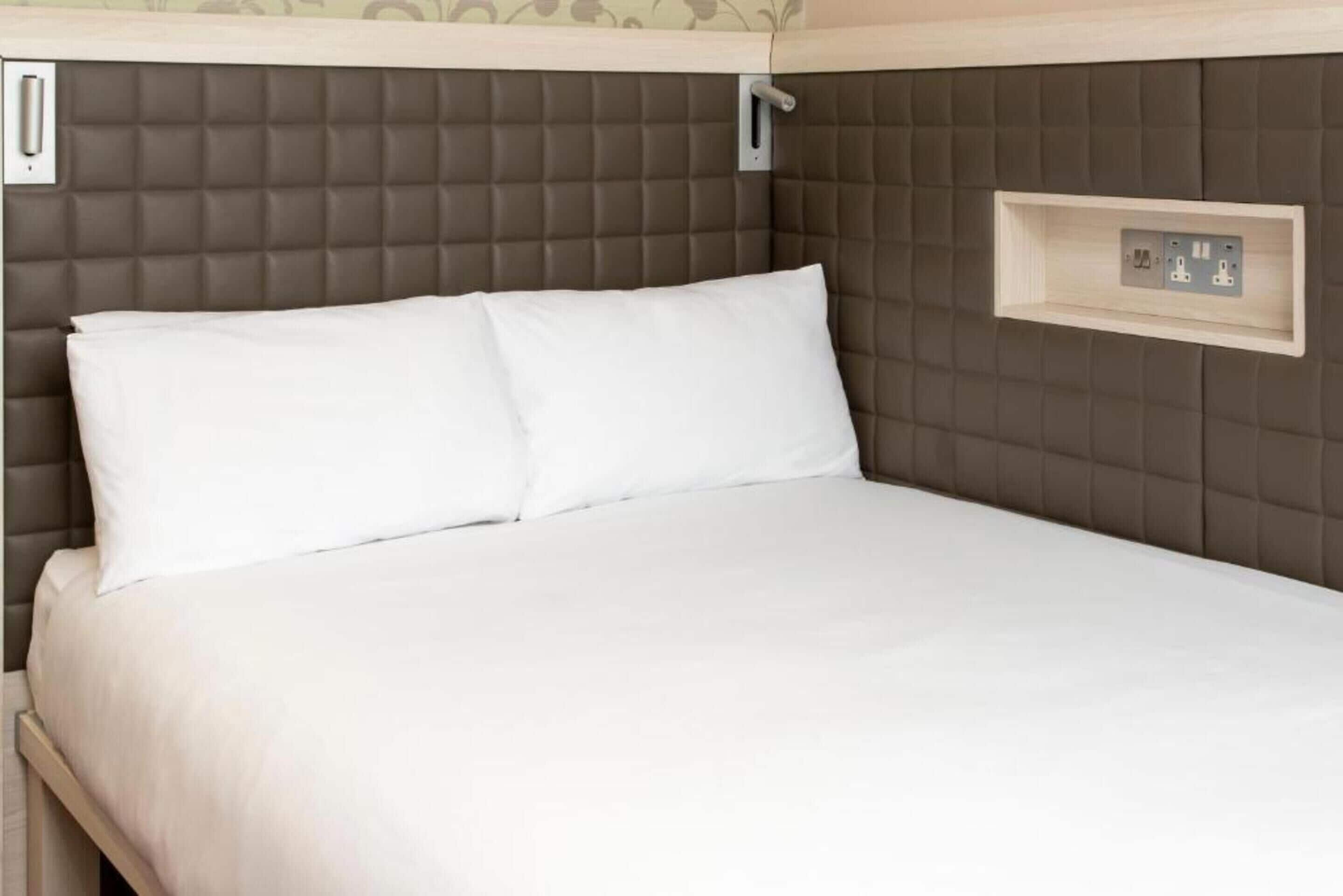 Una cama con cabecera, estante lateral con enchufes y un interruptor de luz en la pared.