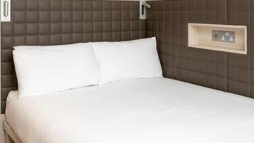 A bed with a headboard, a bedside shelf with electrical outlets, and a wall-mounted light switch.