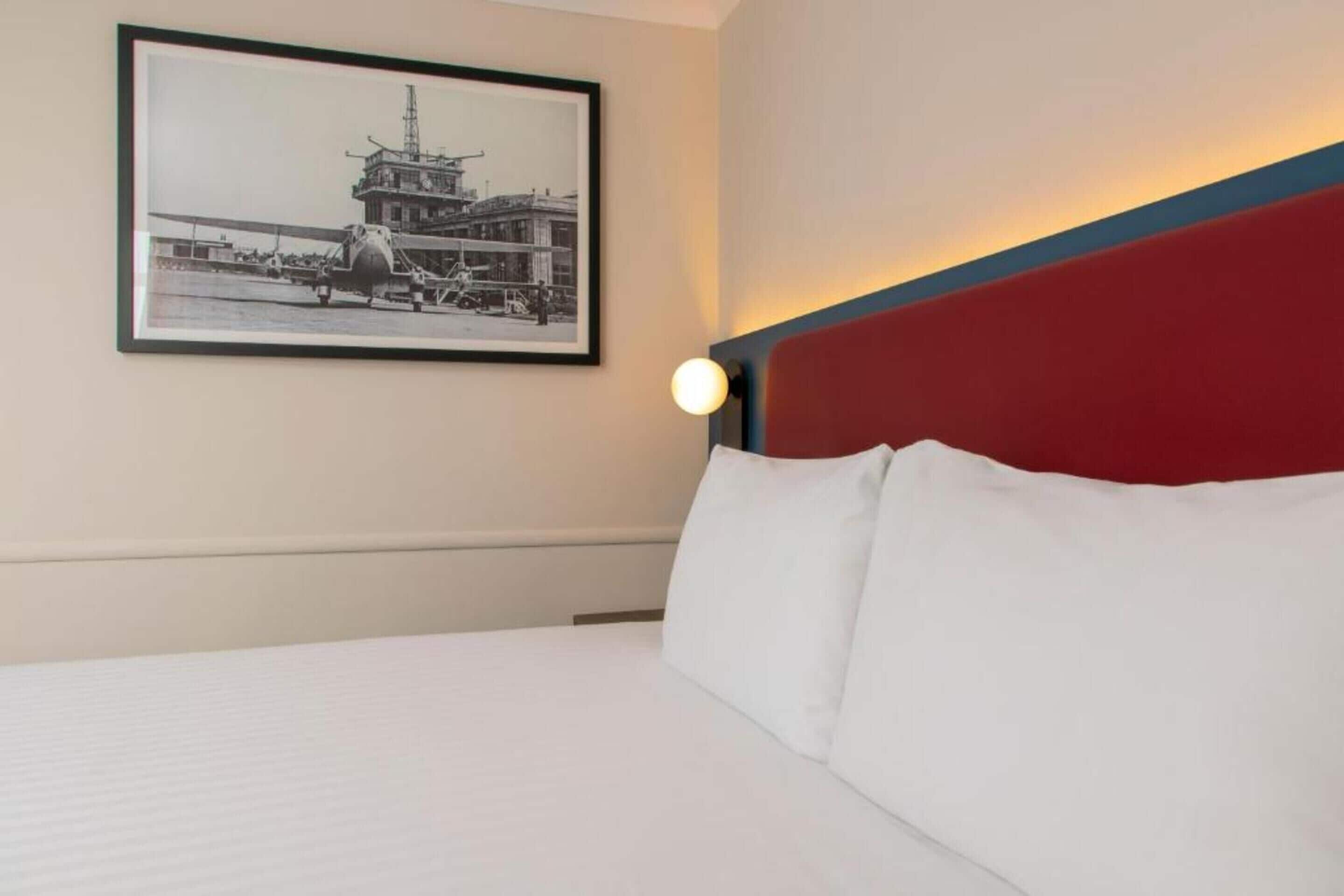 A hotel room with a bed, a framed picture on the wall, and a night light.
