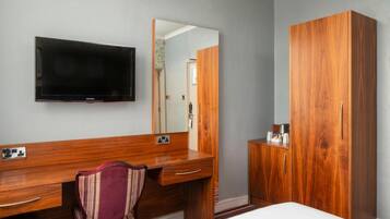 Ein Hotelzimmer mit Holztisch, Wandfernseher, großem Spiegel, Kleiderschrank und Bett.