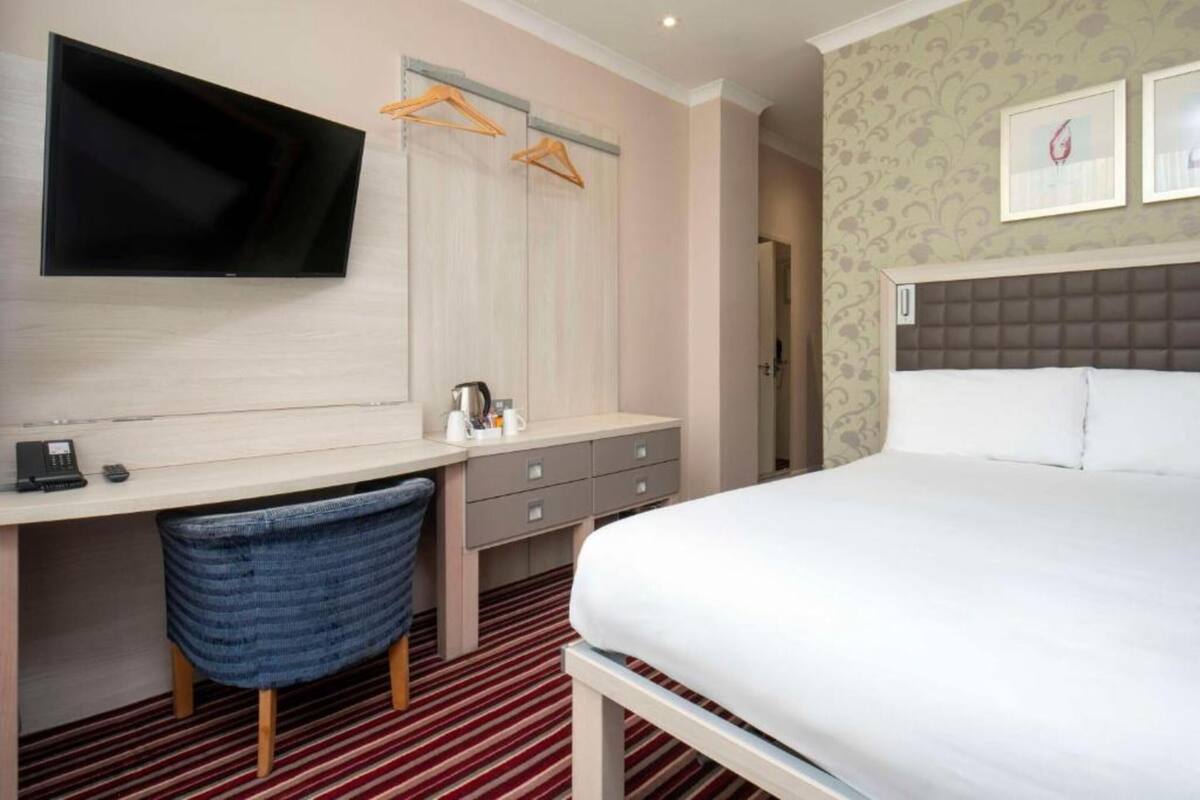 Una camera d'albergo con un letto, una scrivania con una sedia, una televisione e un armadio.