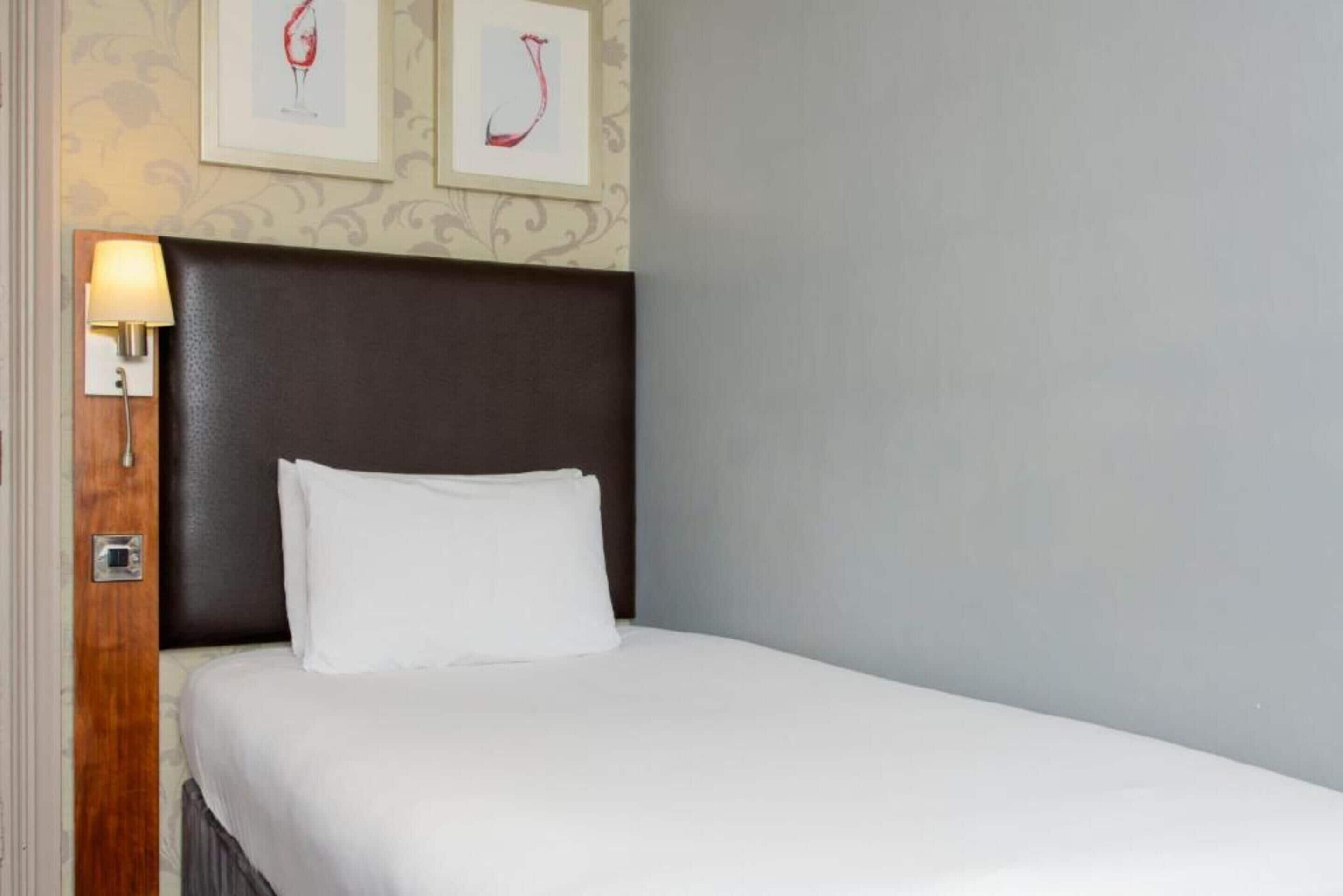 A hotel room with a bed, a nightstand, a lamp, and two framed pictures on the wall.