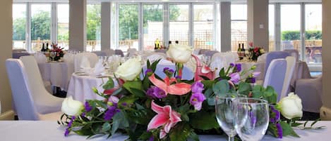 A dining area with tables set for a meal, featuring floral centerpieces and wine glasses.