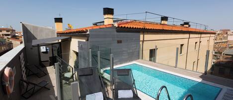 A rooftop pool area with lounge chairs and a clear view of the cityscape.