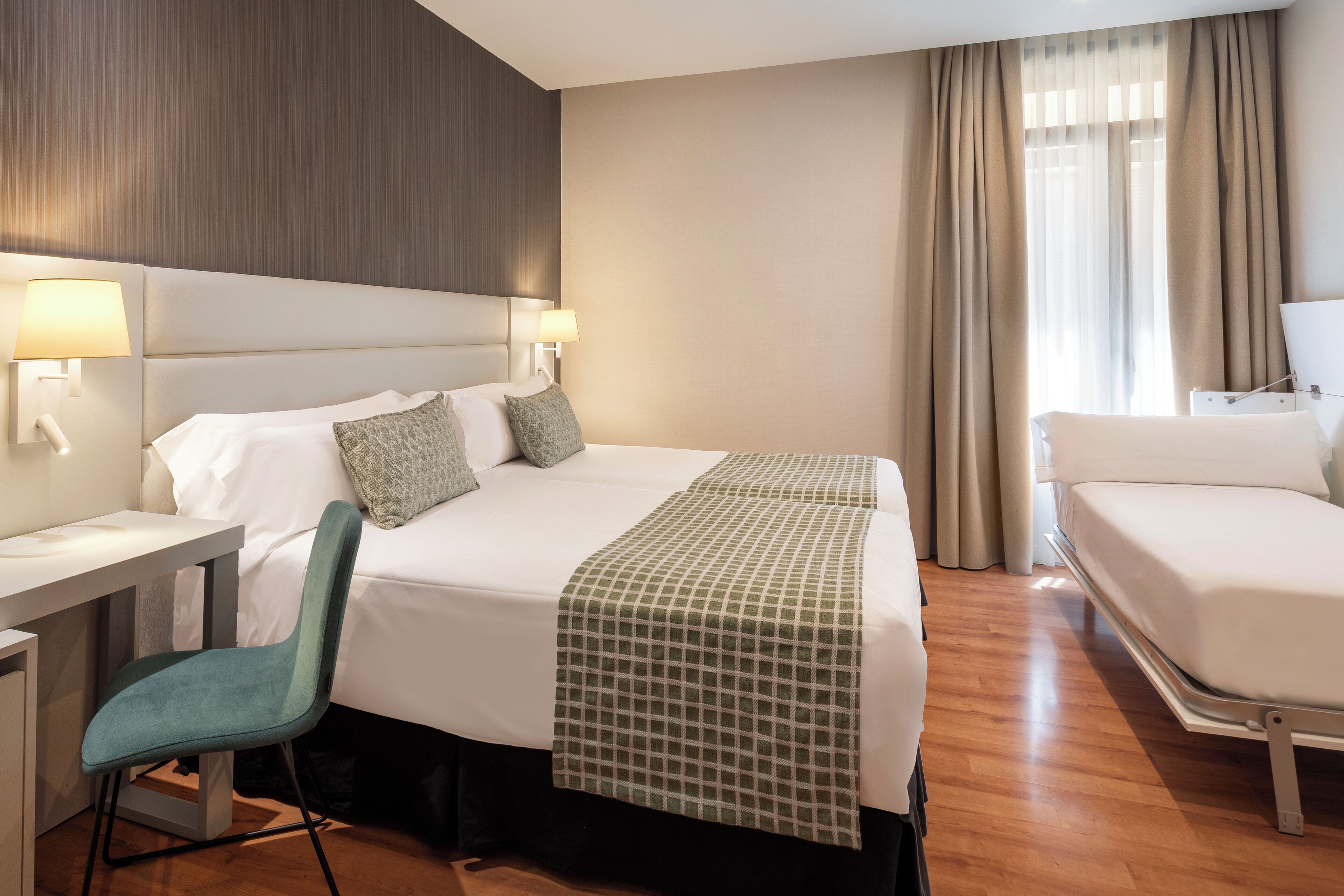 Ett hotellrum med en stor säng, ett skrivbord, en stol och ett fönster med gardiner.