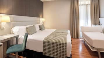 Una habitación de hotel con una cama grande, un escritorio, una silla y un ventanal con cortinas.