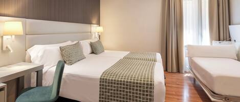 A hotel room with a large bed, a desk, a chair, and a window with curtains.