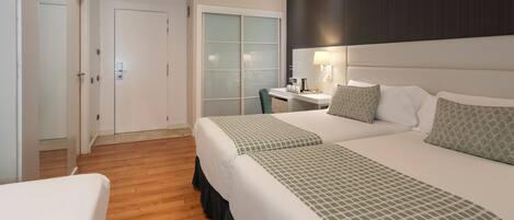 Habitación de hotel con dos camas, un escritorio y una silla. Se ve una puerta y una ventana con persianas.