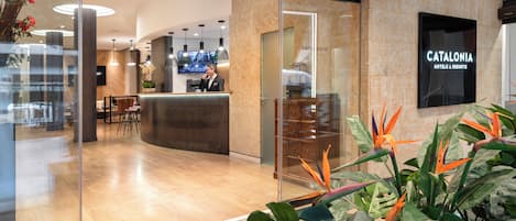 Eine moderne Hotelhalle mit einer Rezeption, einer Sitzecke und einem großen Schild für Catalonia Hotels & Resorts.