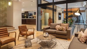 A modern lobby with leather sofas, a reception desk, and a glass wall offering a view of the interior. - Catalonia Plaza Mayor Salamanca (Salamanca)