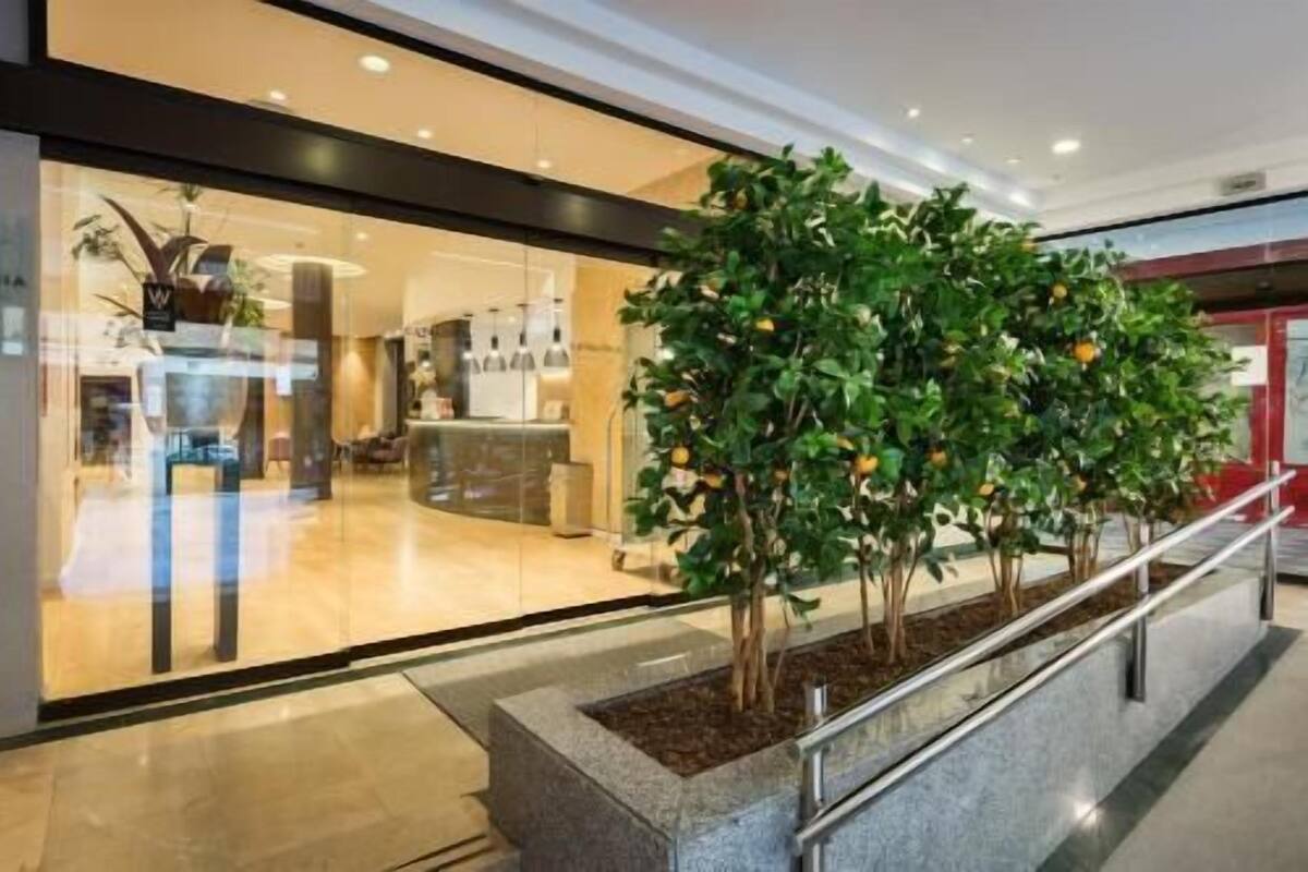A modern indoor space with a reception desk, seating area, and a row of artificial trees with orange fruits.