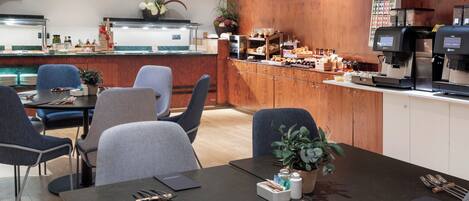 Comedor de hotel con bufé, disposición de mesas y máquinas de café.