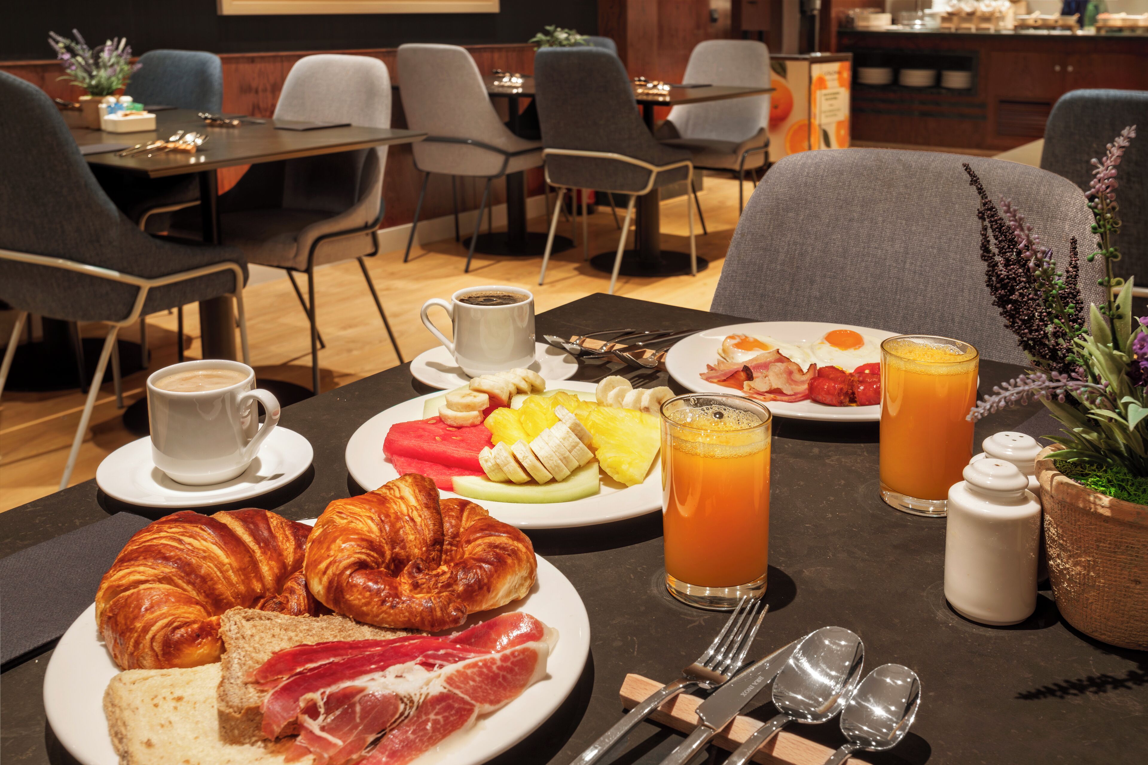 Una mesa con croissants, frutas, embutidos, café y zumo de naranja para el desayuno.