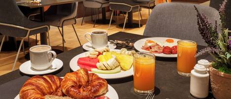 A breakfast setting with croissants, fruits, meats, coffee, and orange juice on a table.