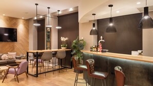 A modern bar area with a wooden floor, leather bar stools, a long counter, and pendant lighting. - Catalonia Plaza Mayor Salamanca (Salamanca)