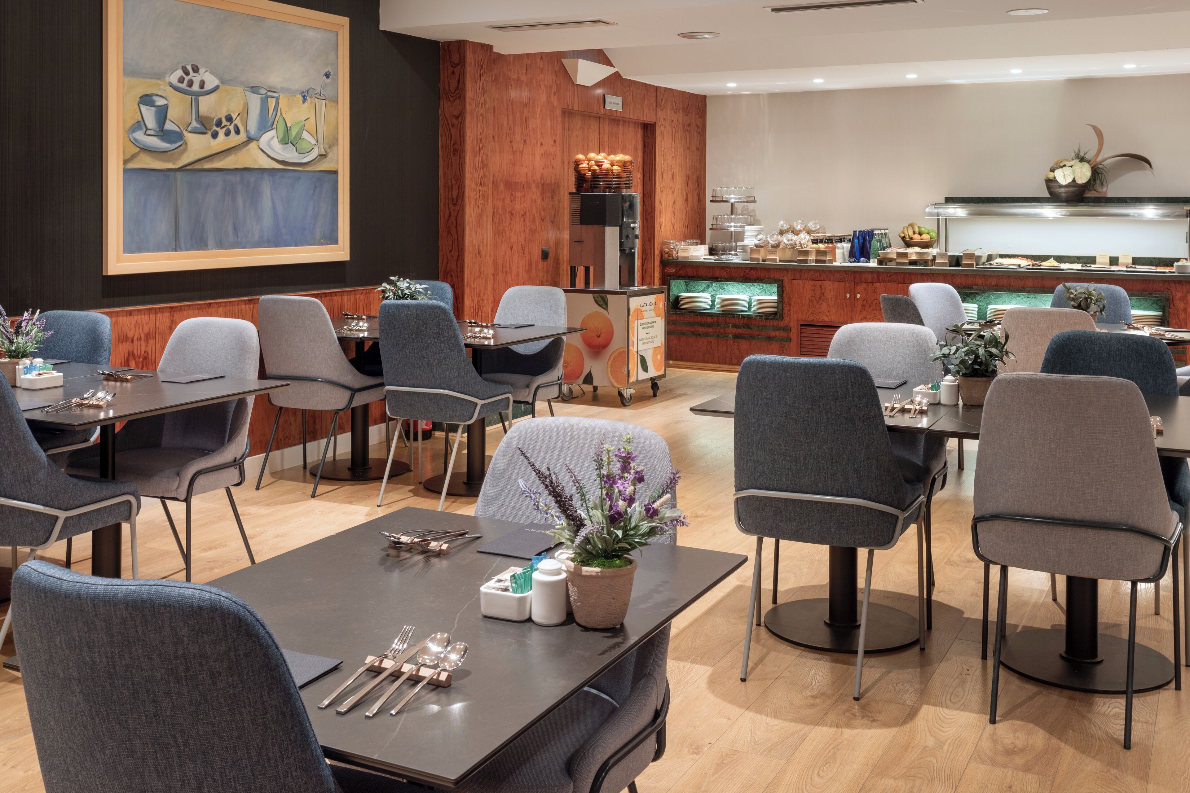 Ein Restaurant mit mehreren Tischen und Stühlen, einem Küchenbereich und einem großen Gemälde an der Wand.