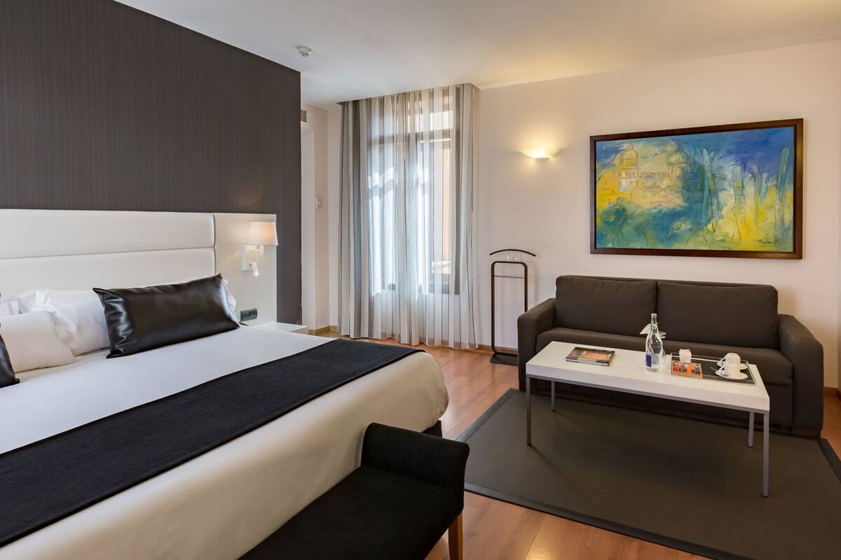 A hotel room with a bed, a sofa, a coffee table, and a painting on the wall.