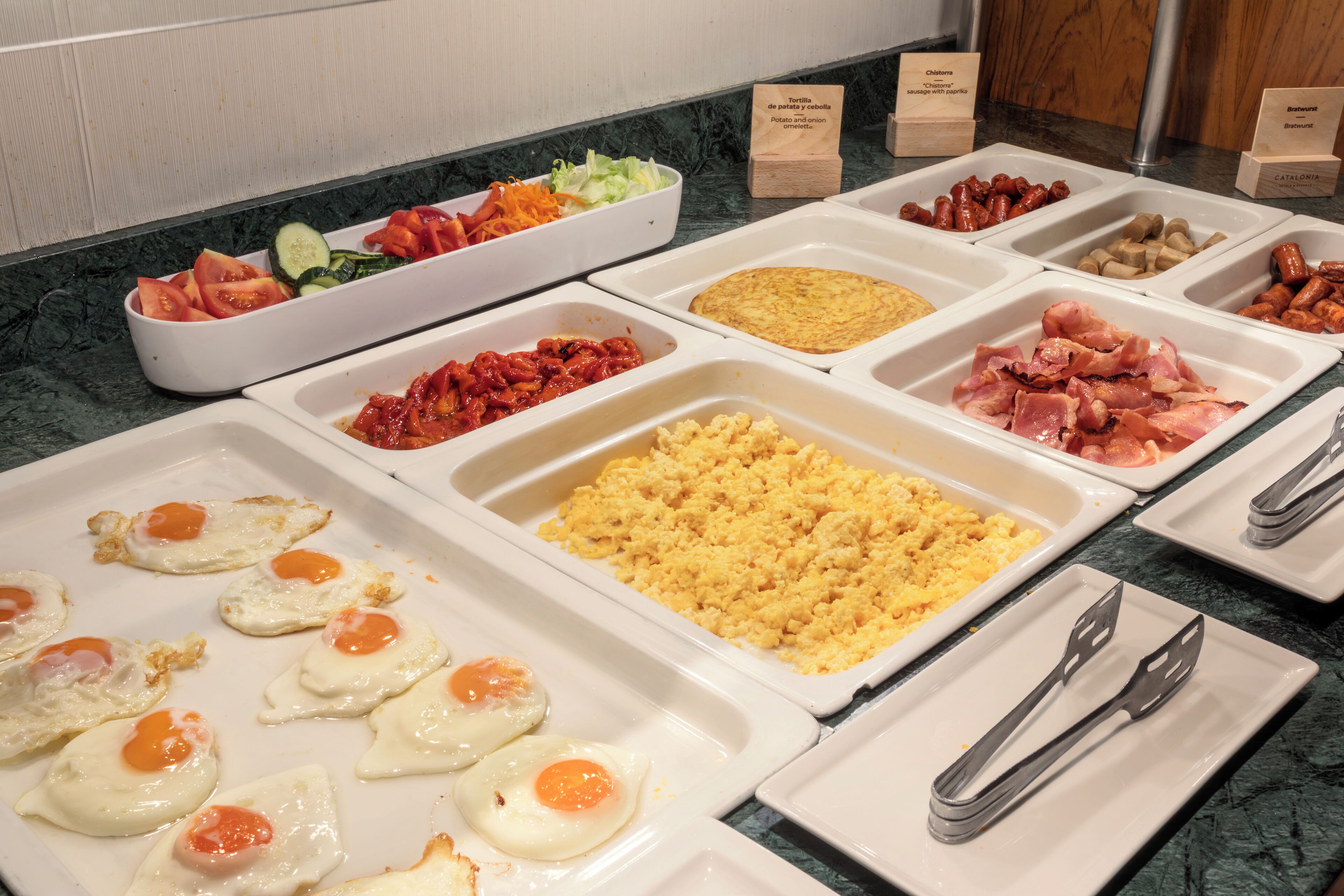 Un bufé con diversas opciones de comida, incluyendo huevos, huevos revueltos y diferentes carnes.