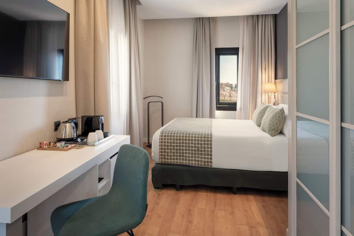 A hotel room with a bed, a desk, a chair, a TV, and a window with curtains.