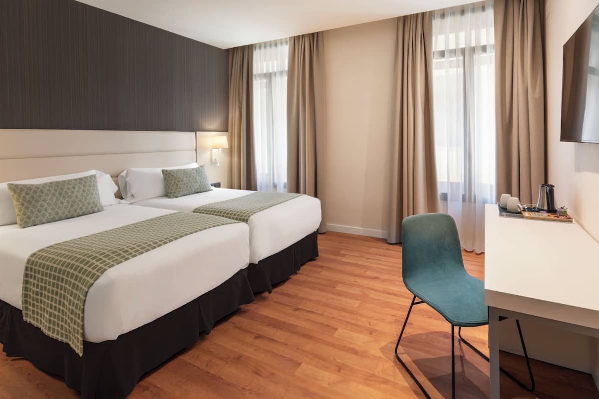 A hotel room with two beds, a desk, and a chair.