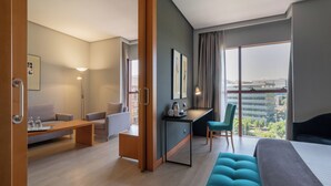 Quarto de hotel moderno com cama, escrivaninha, sofá e vista para a cidade.