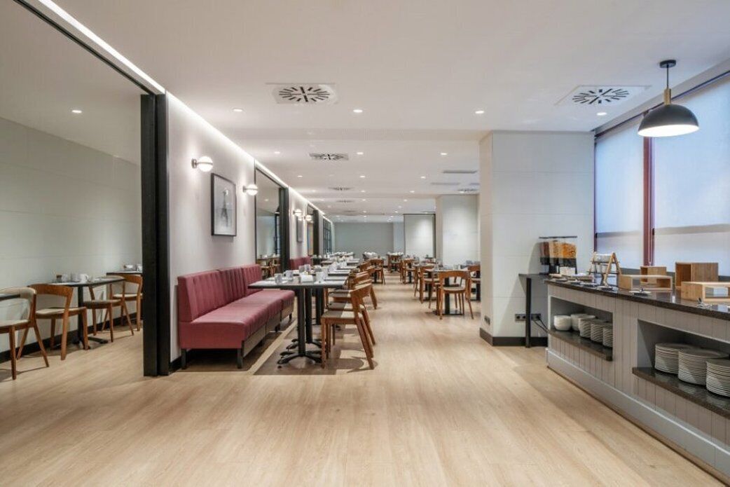 A modern dining area with wooden tables and chairs, a red bench, and a buffet counter with plates.