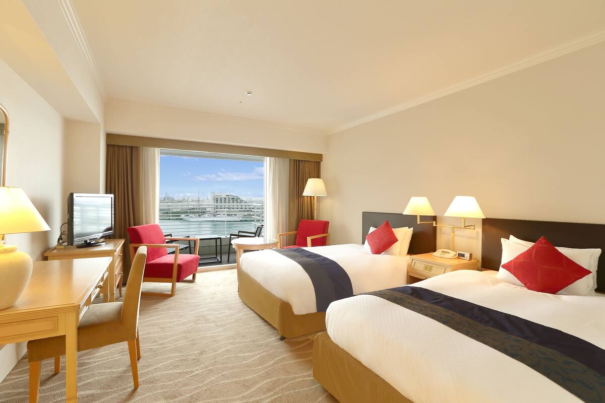 Habitación de hotel con dos camas, un escritorio, una silla, un televisor y vistas de la ciudad.