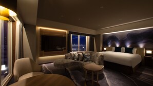 A modern hotel room with a curved sofa, a round table, a bed, and a view of the city at night. - Kobe MerikenPark Oriental Hotel (Kobe)