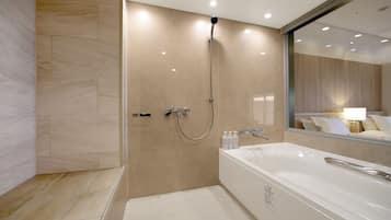 A modern bathroom with a walk-in shower, a large bathtub, and a mirror reflecting a bed with pillows.