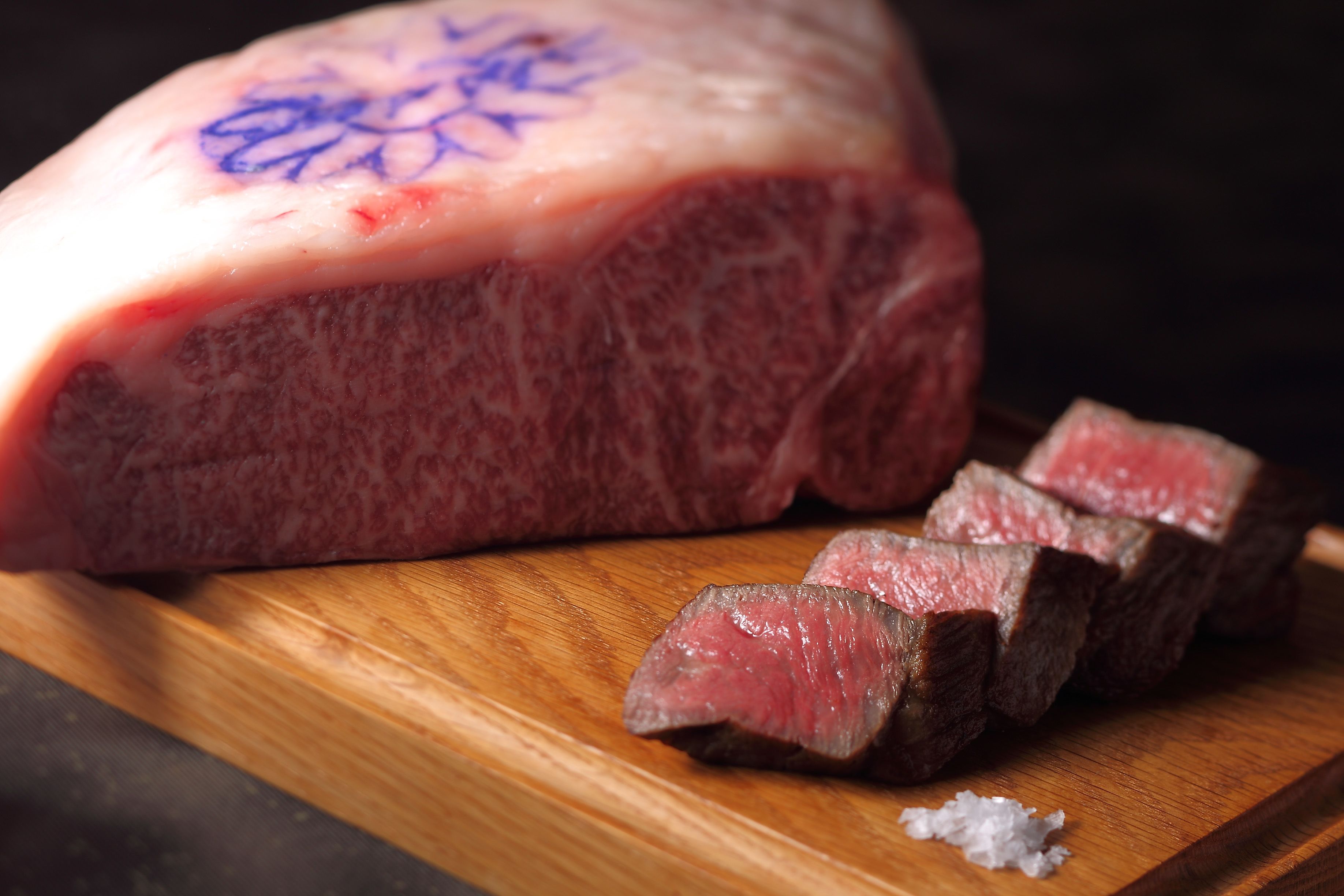 A large piece of meat with a bone, sliced into several pieces, on a wooden cutting board.