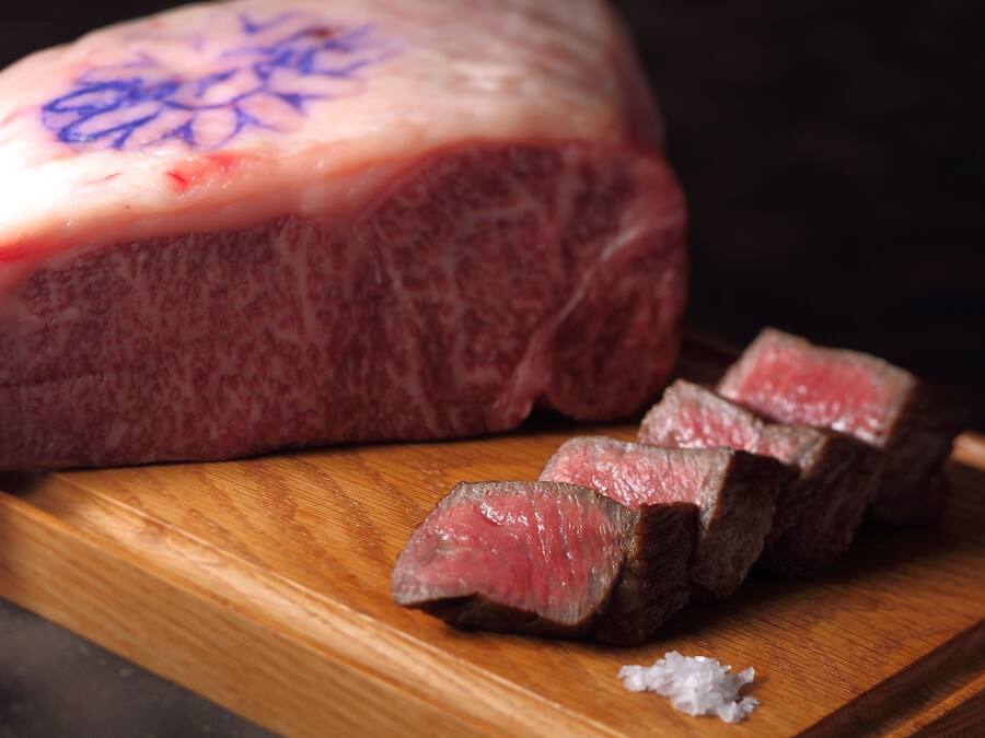 A large piece of meat with a bone, sliced into several pieces, on a wooden cutting board.