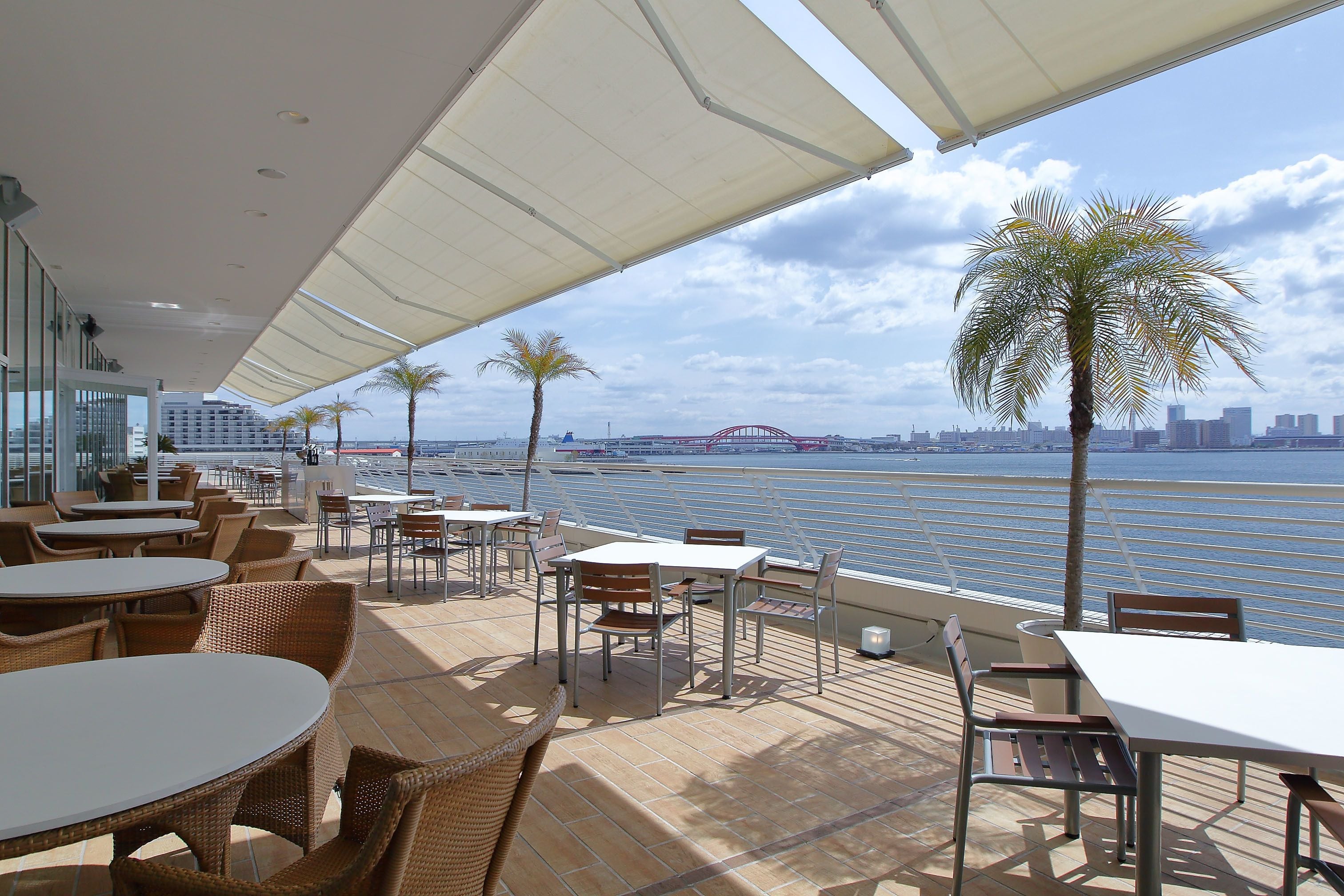 An outdoor dining area with tables and chairs, overlooking a body of water and a city skyline.