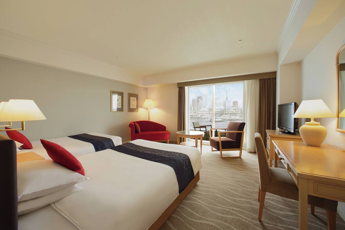 Habitación de hotel con dos camas, un escritorio, una silla, un televisor y vistas a la ciudad.