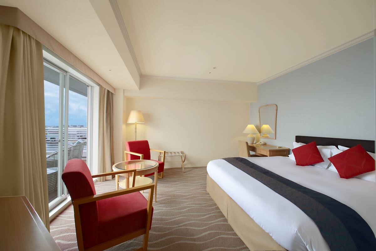 Una habitación de hotel con una cama grande, un escritorio, una silla, una mesita y una ventana con cortinas.