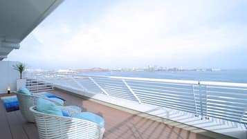 A deck with white wicker chairs and a view of the sea and a bridge.