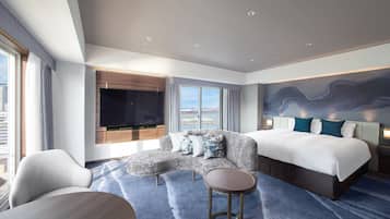 A modern hotel room with a curved sofa, a round coffee table, a large bed, and a flat-screen TV mounted on the wall.