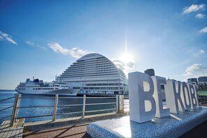A cruise ship docked at a port with a modern hotel in the background. - Kobe MerikenPark Oriental Hotel (Kobe)